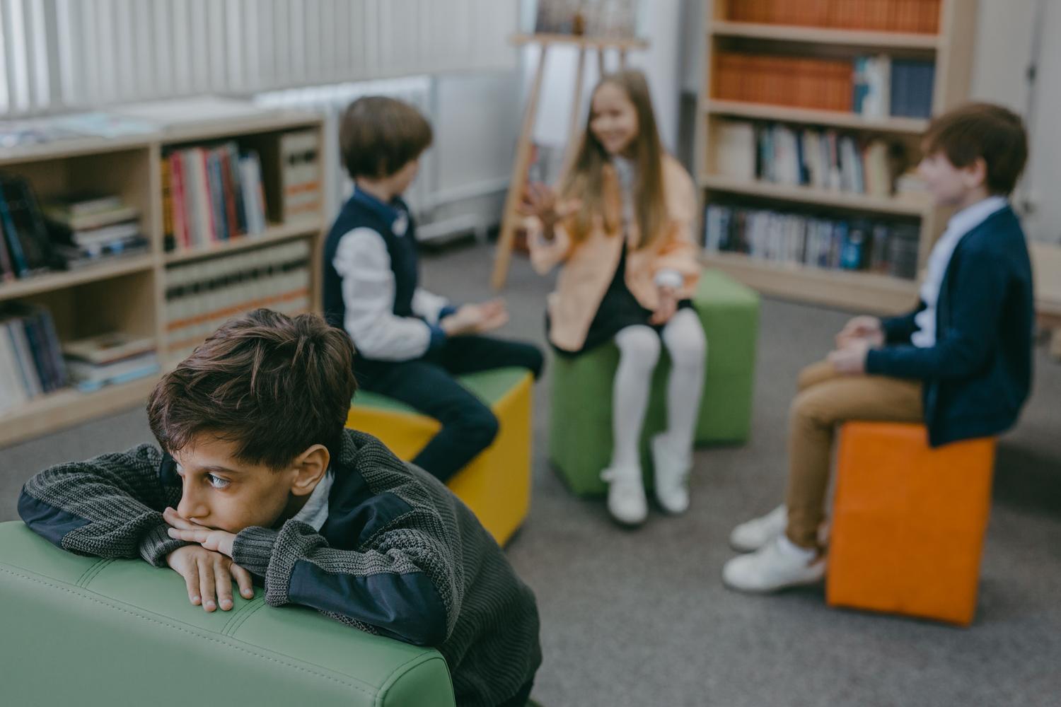 Niño aislado y triste en una biblioteca escolar, representando la necesidad de detección de crisis emocionales.