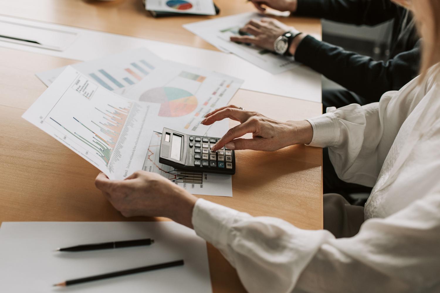 Primer plano de una persona utilizando una calculadora para analizar datos financieros y gráficos en una reunión.