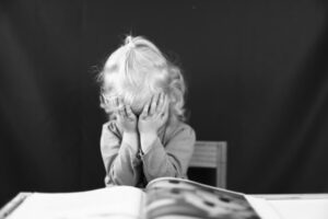 Niño frustrado cubriendo su rostro con las manos frente a un libro, representando la lucha emocional y el sentimiento de superación ante la dislexia
