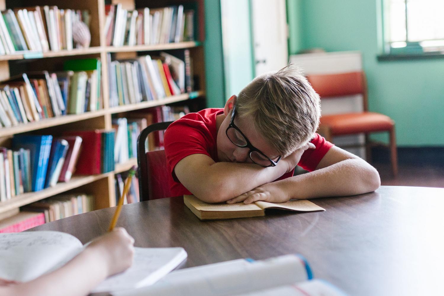 Niño dormido sobre un libro en la biblioteca, reflejando la energía cognitiva agotadora que produce la lectura en personas con dislexia