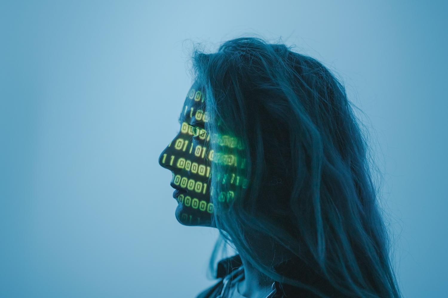 Silueta de una mujer con código binario en el rostro, ilustrando la fusión entre la biología humana y los algoritmos sintéticos.