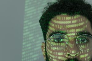 Hombre con código binario proyectado en su rostro, simbolizando la manipulación de la identidad mediante inteligencia artificial.