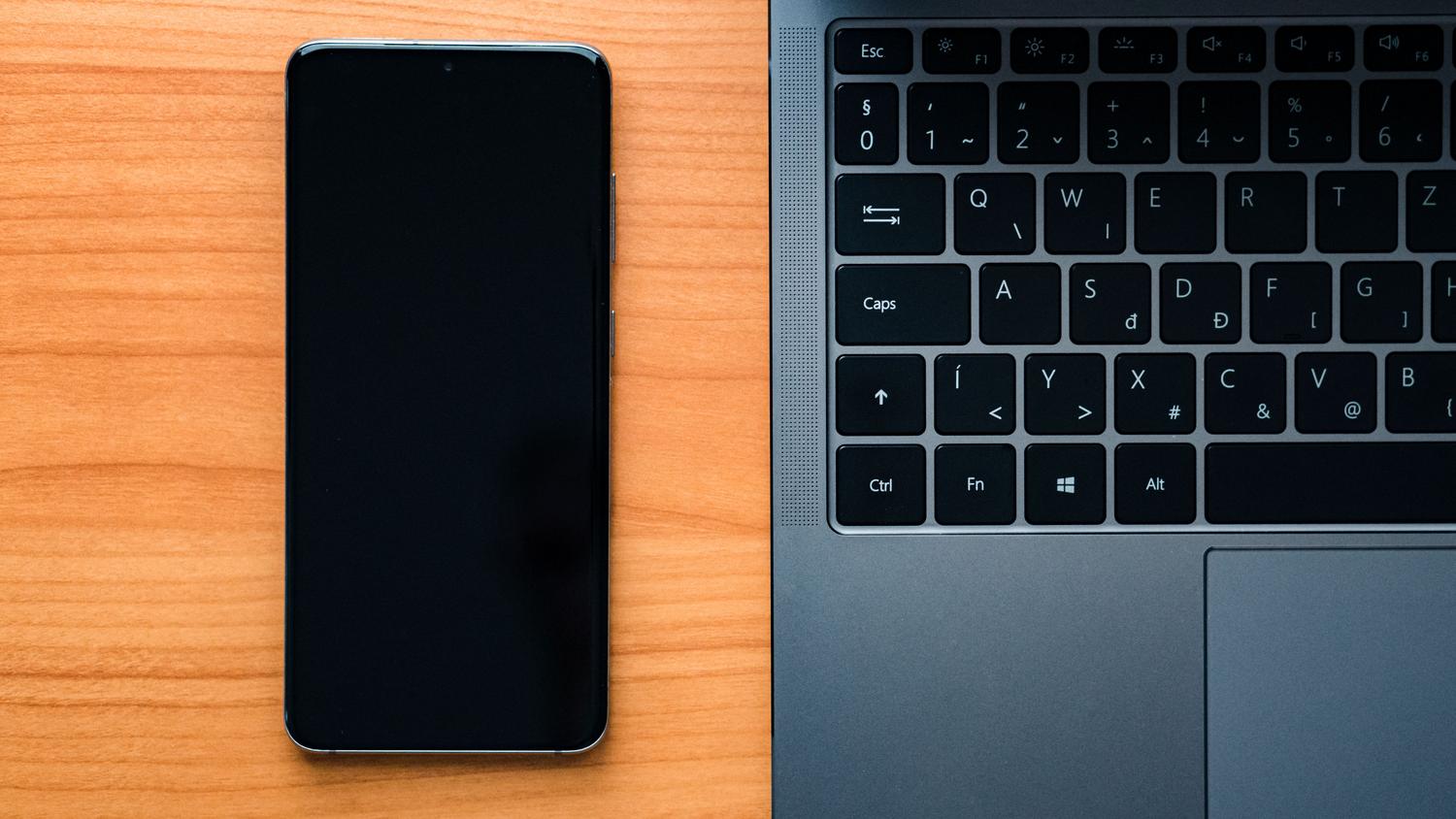 Laptop y smartphone sobre un escritorio de madera, representando el acceso al área de cliente de un operador de telefonía.