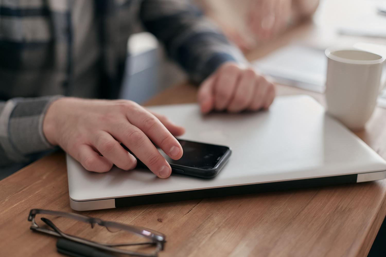 Persona utilizando simultáneamente un smartphone y un ordenador portátil, representando el uso de software de recuperación de datos mediante conexión USB.
