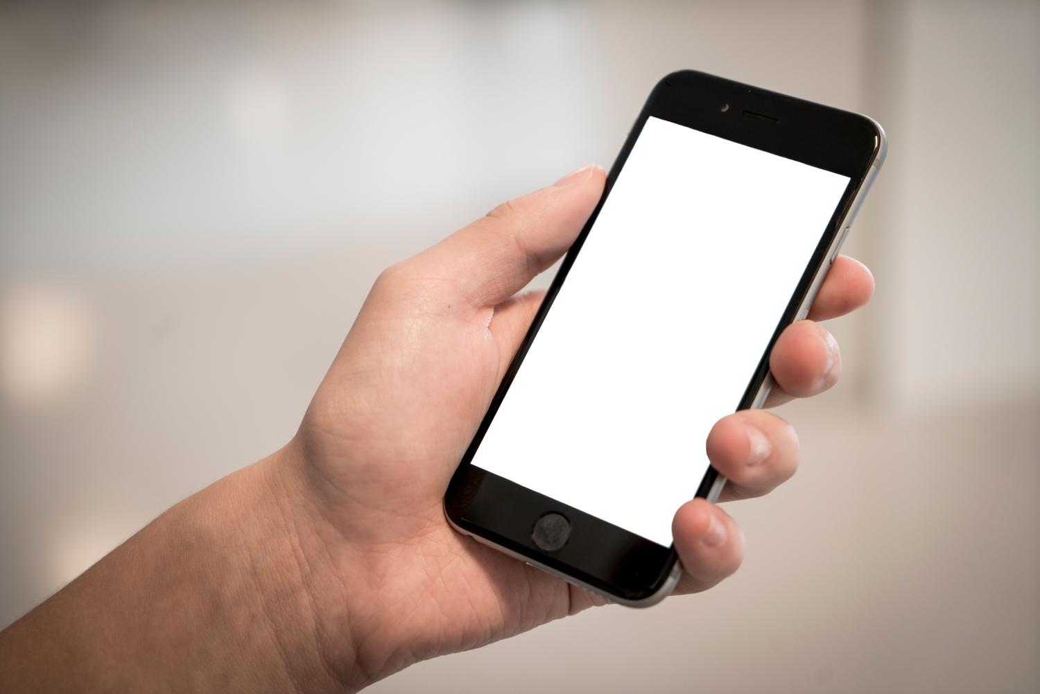 Persona sosteniendo un smartphone moderno con pantalla blanca, representando la interfaz de un sistema operativo.