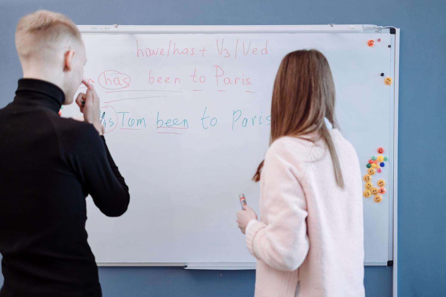 Profesor y alumno estudiando gramática frente a una pizarra en un aula, ilustrando el proceso de aprendizaje colaborativo.