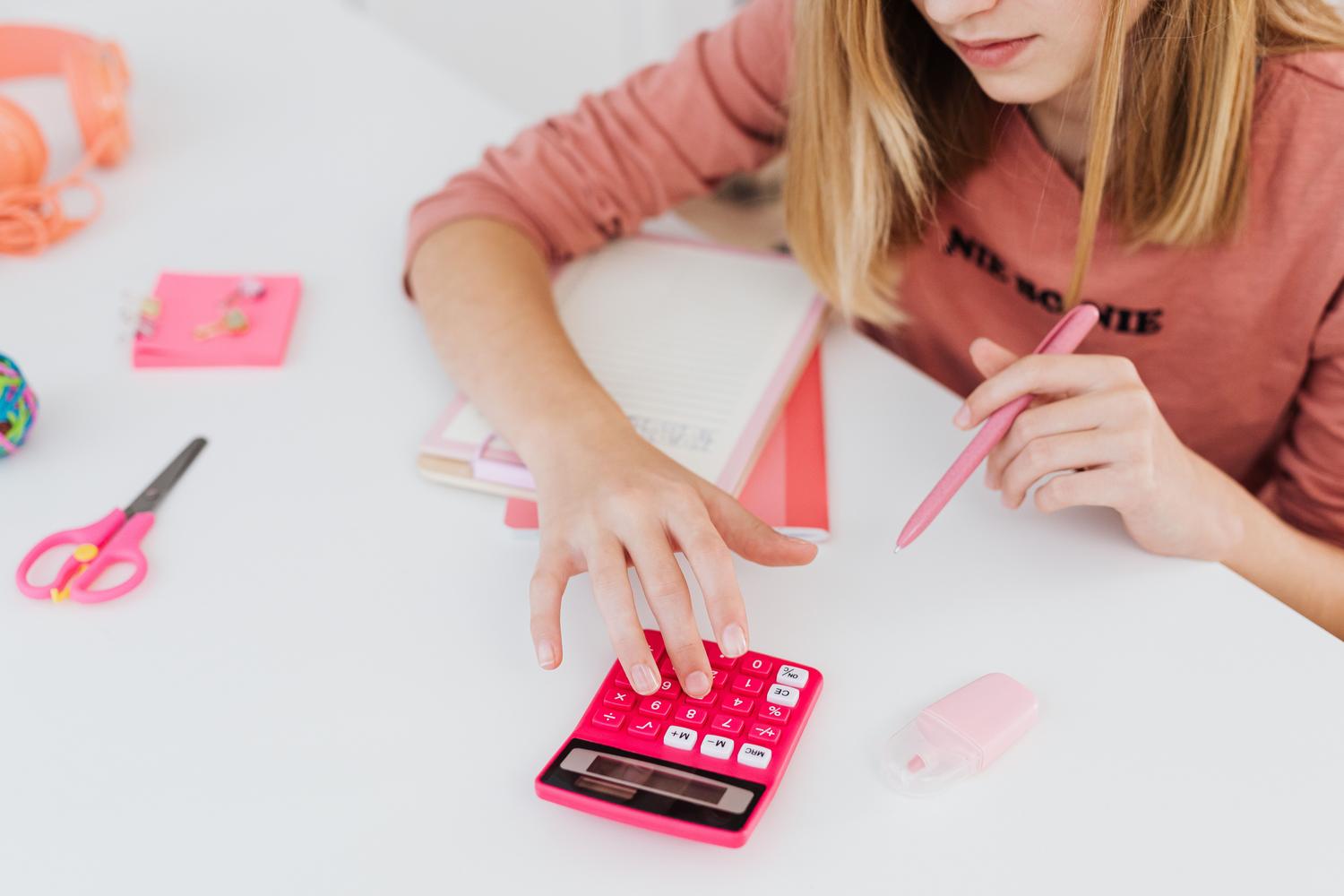 Niña de primaria usando una calculadora rosa en un espacio de estudio luminoso y organizado.